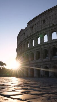 Rome, Italy - March 18, 2026: (Vertical Video) Roman Colosseum at Sunrise Beautiful Start Burst Lens flare. A Male Photographer Walks Across Frame