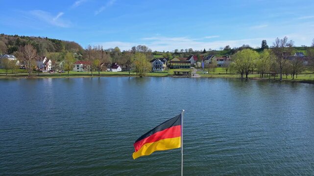 Die deutsche Flagge weht vor einem Hintergrund eines Waldes und eines blauen Himmels im Wind, Gro&szlig;er Brombachsee, Fr&auml;nkischen Seenland, Landkreis Wei&szlig;enburg-Gunzenhausen, Mittelfranken, Bayern, Deutsc