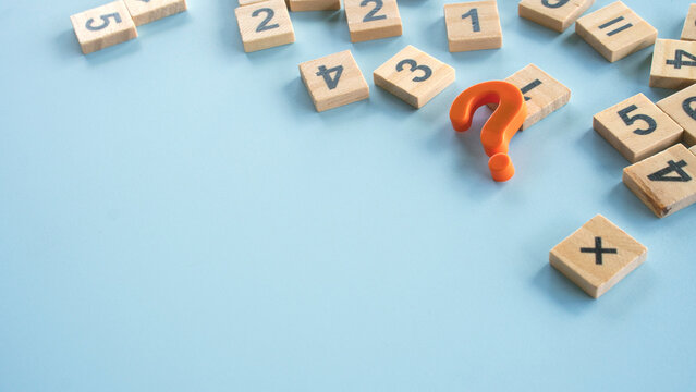 Orange question mark symbol with scattered wooden number tiles on blue background concept for mathematics problem solving or quiz