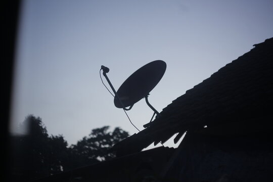Silhouette of a satellite dish on a house roof against a clear evening sky.