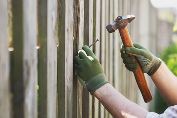 Male hands drive nail with hammer tool in wooden fence plank, maintenance repair, diy and carpentry...