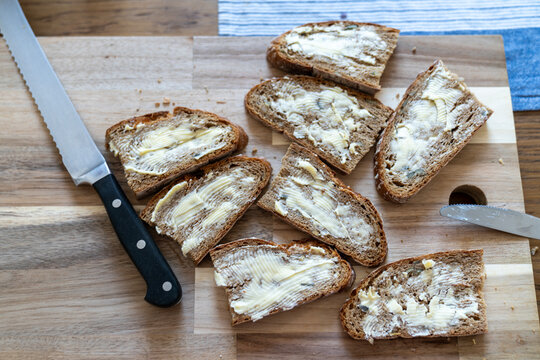 Top view of buttered rye bread slices on a wooden cutting board with a bread knife