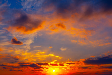 Fototapeta premium Sunset blazes across sky with the sun glowing near horizon, casting gold hues over dramatic clouds. Deep blue and purple tones contrast beautifully with twilight