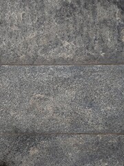 Fototapeta premium Texture of dark gray coarse granite natural stone tile surface with horizontal boundary joints for outdoor flooring or architectural wall materials.