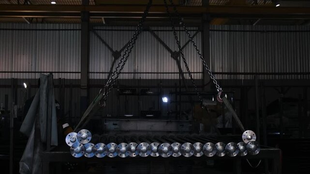 Steel pipes with flanges being lifted by crane slings in industrial workshop, material handling process, 4K