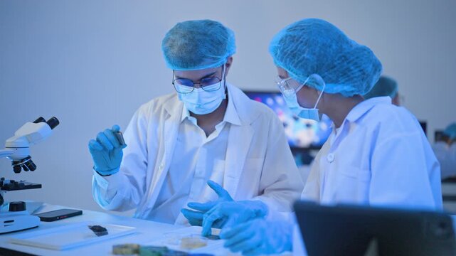Two masked researchers point to and study a specimen vial beside a microscope in a cinematic blue lab, suited to biotech, diagnostics and discovery themes.