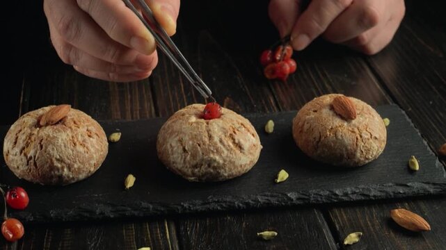 Hands carefully placing red berries on baked goods topped with almonds on a slate board, showcasing meticulous food preparation in a cozy kitchen setting
