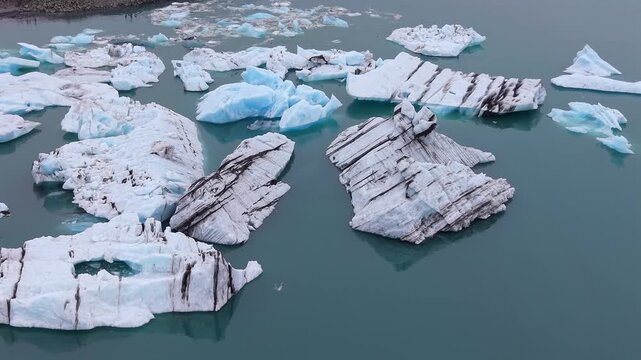Stunning aerial view of blue and white icebergs, some with volcanic ash stripes, drifting slowly in the calm, green water of the famous lake
