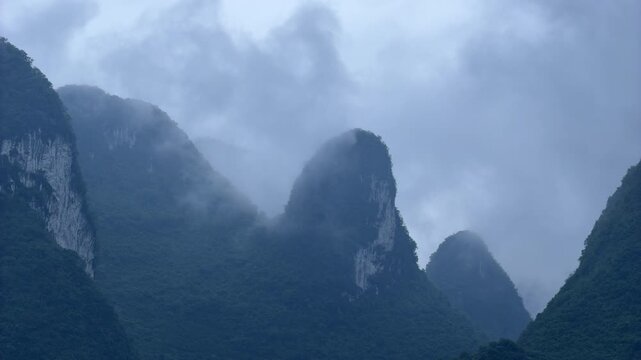 Timelapse showing the movement of heavy white mist and foggy clouds swirling around the towering karst mountain peaks in the scenic landscape of Guilin, Guilin, China. Atmospheric weather and nature 