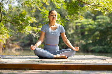 Fototapeta premium Yoga woman meditation outdoor nature sitting calm exercise woman practicing yoga meditation sitting outdoor on wooden platform surrounded by green forest sunlight