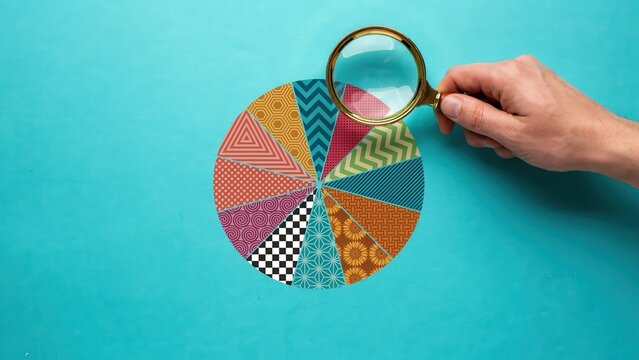 A hand holding a magnifying glass examines a colorful pie chart on a blue background.
