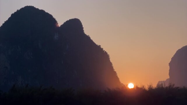 Time lapse of beautiful golden sunset with sun setting behind dramatic karst mountain silhouettes in China