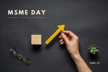 Fototapeta premium A hand holding a yellow arrow pointing up near a block and glasses on a desk for MSME Day