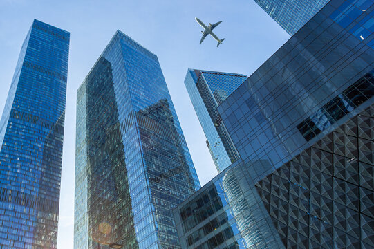 Modern glass skyscrapers on a clear day and passenger plane flying over