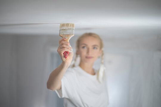 Detailed close up of hand holding paint brush against ceiling with copy space