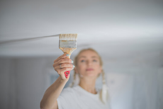 Detailed macro shot of paint brush applying white color on ceiling with copy space