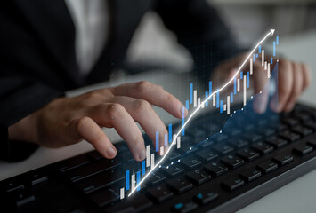 Fototapeta premium A businessperson engages in financial data analysis using a keyboard, with a digital graph overlay showing upward growth in a contemporary office setting. Impute
