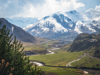 Fototapeta premium Snow-capped peaks rise above lush green valleys, Kazbegi region.