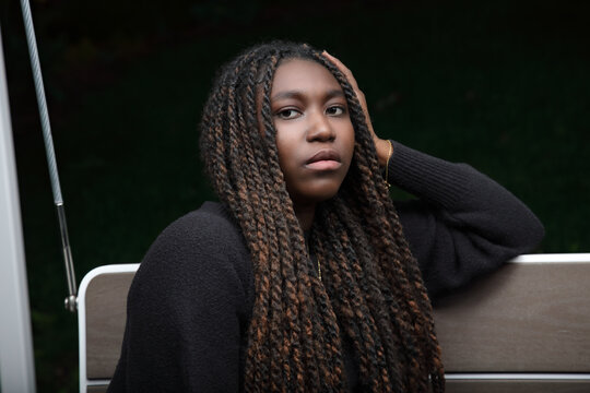 Moody night portrait of a calm young Black woman with long braids resting on a porch swing