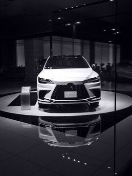 A white Lexus RX 500h luxury SUV on a rotating showroom display stand, shot in monochrome style through a glass window