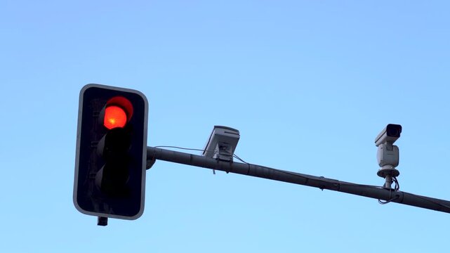 Detalle de un sem&aacute;foro cambiando de color junto a varias c&aacute;maras de vigilancia y control del tr&aacute;fico, con un cielo azul despejado de fondo.