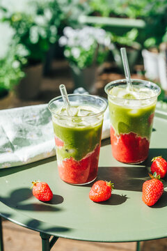 Two glasses of strawberry matcha latte on a sunny balcony table. Trendy layered beverage and healthy lifestyle concept