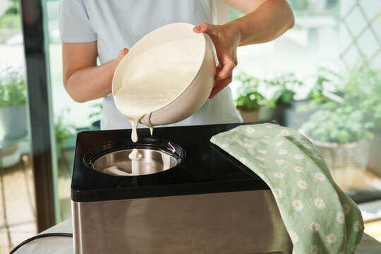 Pouring creamy ice cream mixture into an ice cream maker. Homemade frozen dessert preparation process