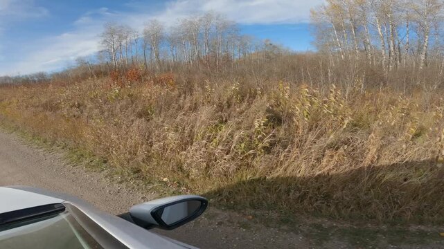 POV looking out the window of a white car while driving through dry grassy prairie landscape with white sky in the blue sky
