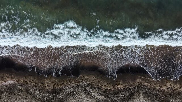 Waves roll gently onto the shore at sunset, creating a white foam over the sand. The sky shows colors as day turns to night. Birds fly above the water, enjoying the coastal scene.