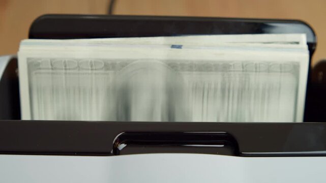 In a bright office, bills are fed into a sleek money counting machine, showcasing its swift and precise counting abilities for financial tasks