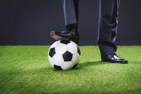 a sporty man in an elegant suit with soccer ball in big stadium - coach or professional player concept. Feet of soccer coach, player step on soccer ball.