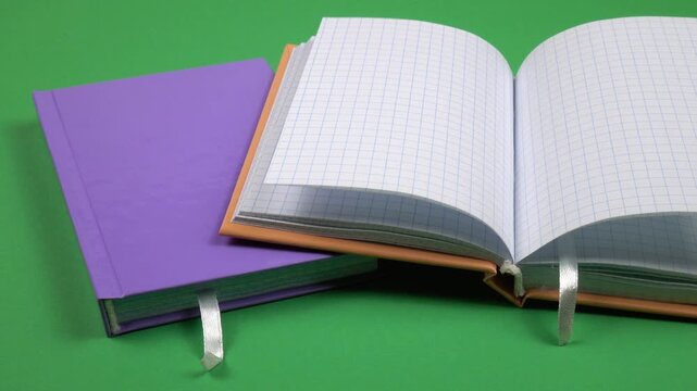 Notebooks with colorful bindings are on a green background. The pages of an open notebook sway in the air.