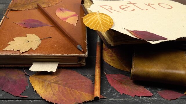 Various types of vintage notepads and dried autumn leaves lie on a black table, family archive, memories.