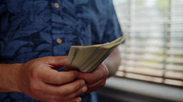 Hands gently manipulate fresh bills, savoring the moment of counting money in a warm room filled with sunlight on a tranquil afternoon
