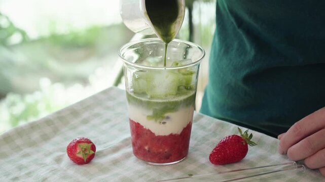 lose-up of trendy strawberry matcha latte being prepared in a glass. Layered drink with strawberry puree, milk and green matcha tea. Healthy lifestyle and modern cafe beverage concept