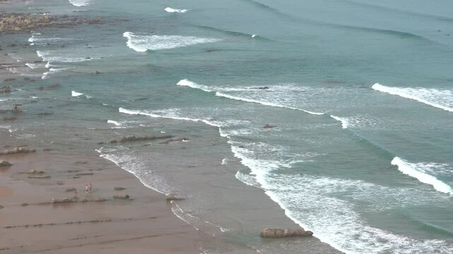 Surfers on waves at the flysch rock beach in zumaia, basque country