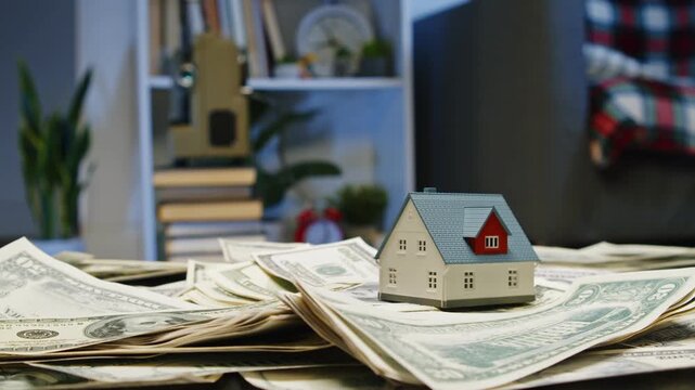Small houses sit atop stacks of money, representing dreams of financial security and homeownership. This creative perspective invites viewers to reflect on wealth and futures
