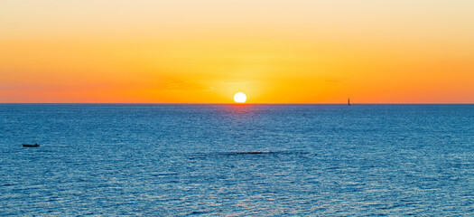 Fototapeta premium Golden sunrise over the vast ocean horizon with a sailboat and small boat