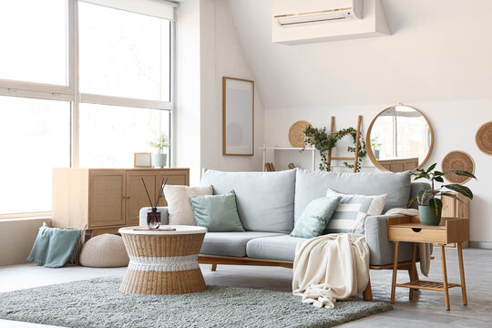 Interior of living room with sofa, wicker coffee table, houseplants and commode near window