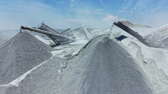 A granite quarry site features large machinery processing stone. Piles of granite material are visible. Dust is present in the air, indicating active work at the site.