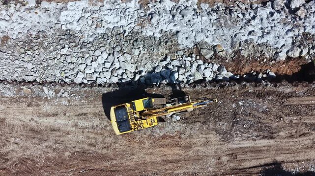 Heavy machinery is working on a construction site. The excavator is moving large rocks and dirt in the afternoon. The ground shows signs of recent digging and earthmoving.