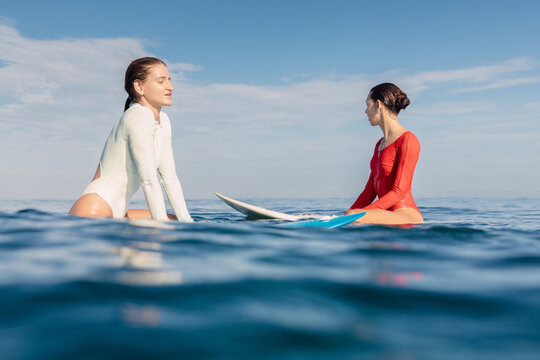 Two girl surfers sitting on surfboards in calm ocean waiting for surfing waves