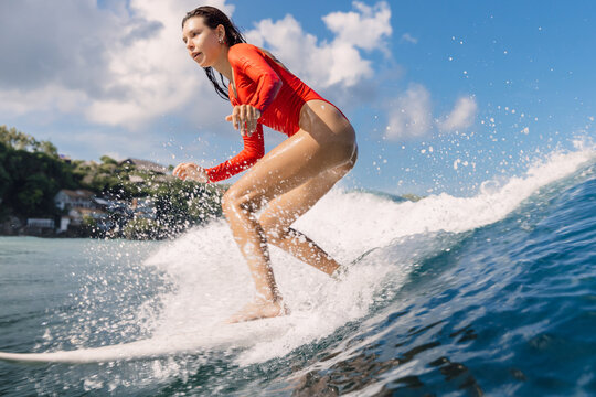Female surfer in swim suit rides wave with splashes in tropical ocean