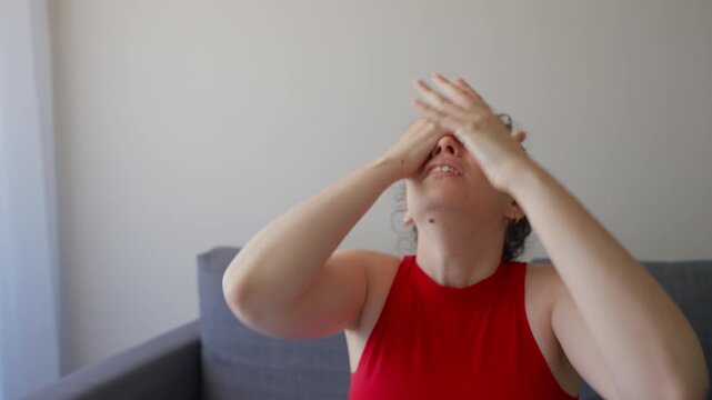 Sports fan watching live match at home is sad and disappointed by score result. Woman sitting on sofa with red face paint and clothes cheering for her favorite team is angry and unhappy with game play