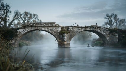 Fototapeta premium Old Stone Bridge Over Calm River with Mist and Trees at Dawn