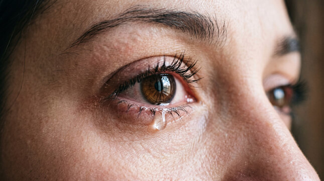 Emotional crying woman with tear drop on face, close-up of brown eye weeping, sad female expression with wet eyelashes and skin