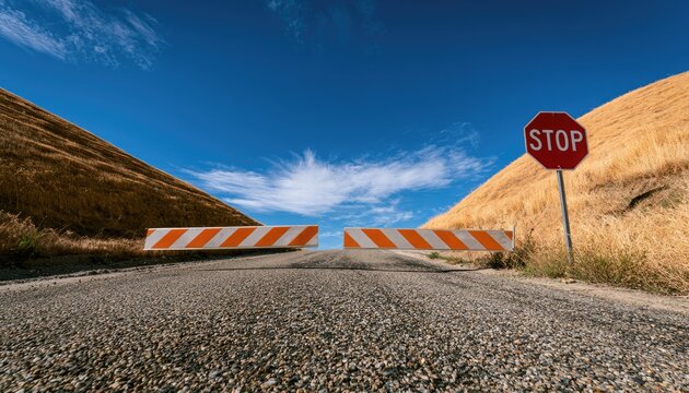 Barricade and stop sign block a desolate road leading to a bright sky