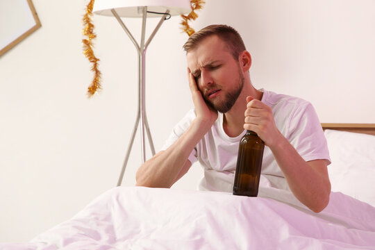 Young man with hangover and beer in bedroom after party