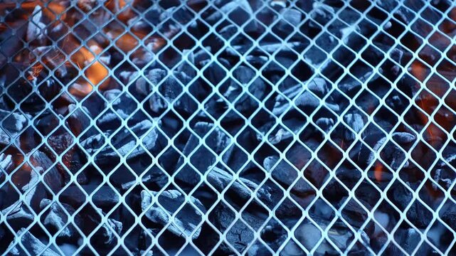 Metal barbecue grill grate with burning charcoal briquettes and orange flames underneath