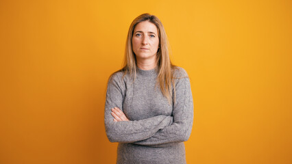 Confident woman with a serious face standing against a yellow background, looking directly at the camera with arms crossed © DMegias